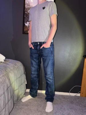 Grå Comme des Garçons PLAY t-shirt - Säljer en grå t-shirt från Comme des Garçons PLAY i storlek S. T-shirten har ett svart hjärta med ögon broderat på bröstet och är i mjuk bomull. Klassisk passform och korta ärmar, perfekt till jeans eller shorts. Storlek S. Personen på bilden är 177. Går att köpa med ett par jenas för bättre pris