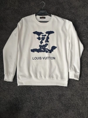 Louis Vuitton sweatshirt  - Vit sweatshirt från Louis Vuitton med mörkblå abstrakt print och logga på bröstet. Tröjan har rund hals, ribbade muddar och är tillverkad i mjuk bomull. Perfekt för dig som gillar stilrena och exklusiva plagg med en twist.