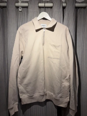 Beige pikétröja från Woodbird - Säljer en stilren beige pikétröja från Woodbird i bomull. Tröjan har lång ärm, klassisk krage, bröstficka med inbroderad logga och half zip-dragkedja framtill. Perfekt för den som gillar en clean och avslappnad look. Storlek M men jag brukar ha L o den passar mig! Knappt använd! (Ordinariepris - 550 kr)!!
