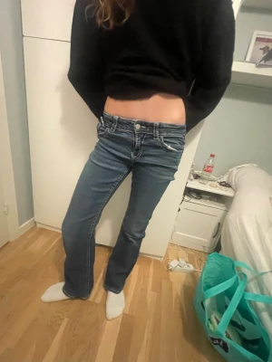 Blå bootcut jeans med låg midja - Säljer ett par blå jeans med snygg bootcut och låg midja. Jeansen har klassiska fickor fram och bak, med coola detaljer på bakfickorna. Perfekta för dig som gillar en avslappnad men trendig look.