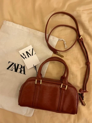 Handväska  - Säljer en snygg liten handväska från Zara. Väskan har både handtag och en justerbar axelrem. Helt oanvänd!