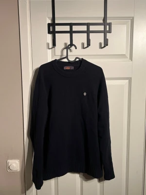 Mörkblå stickad tröja från Morris - Säljer en mörkblå stickad tröja från Morris med rund halsringning och diskret broderad logga på bröstet. Tröjan har ribbade muddar vid ärmslut och nederkant samt lång ärm. Mer frågor eller bilder är det bara att fråga!