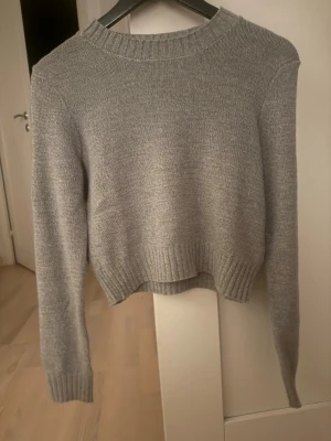 Grå stickad tröja från H&M Divided - Mysig grå stickad tröja från H&M Divided i storlek S. Tröjan har en klassisk rund halsringning, ribbade muddar och är långärmad. Perfekt för lager på lager under kyliga dagar och enkel att matcha till allt.