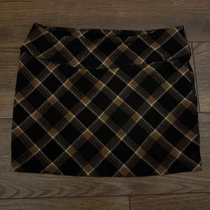 Brun och svart rutig kortkjol - Supersnygg kortkjol med rutigt mönster i brunt, svart och beige. Kjolen har en klassisk rak form och passar perfekt till en cool streetstyle-look. Tjockare tyg som känns stabilt och ger en schysst siluett.