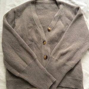 Beige kofta från SHEIN med knappar - Mysig beige kofta från SHEIN i storlek M. Koftan är stickad i polyester, har v-ringning, tre bruna knappar framtill och två fickor. Perfekt för lager-på-lager och chill dagar. Långa ärmar med breda muddar ger en avslappnad vibe. Aldrig använd