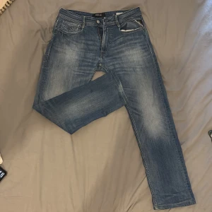 Replay rocco jeans - Säljer ett par klassiska blå jeans från Replay rocco. Jeansen har snygga slitningar och tvättade detaljer, fem fickor och normal midja. Perfekta för dig som gillar en tidlös look med lite edge. Materialet är robust denim som håller länge.