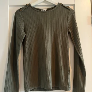 Ribbad grön långärmad tröja XS - Snygg ribbad långärmad tröja i olivgrönt från C. Tröjan har dekorativa knappar på axlarna och är tillverkad i ett mjukt, stretchigt material. 