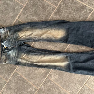 Cheap Monday blå jeans med slitningar - Säljer ett par blå jeans från Cheap Monday med coola slitningar och tydlig tvättad effekt på benen. Klassisk femficksmodell med logga och patch bak. Jeansen är bootcut.