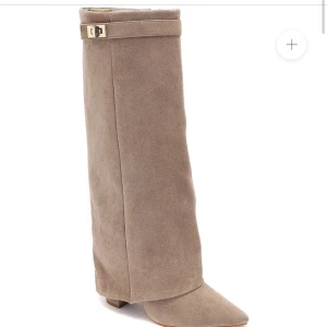 Beiga mockaboots med klack - Snygga höga stövlar i beige mocka med spetsig tå och blockklack. Stövlarna har guldfärgad spänndetalj upptill och dragkedja på insidan för enkel påtagning. Skorna är använda 1 gång och jag tyckte de var sköna att gå i och jag fick inget skav.  