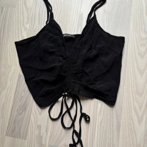 Svart croppad linnetopp Gina Tricot - Svart croppad linnetopp från Gina Tricot med smala axelband och snygg snörning framtill som gör att du kan välja tröjans längd . Toppen har v-ringning och är tillverkad i ett mjukt, lätt material. Skick är jätte svårt att sätta då alla tycker olika men enligt mig är linnet i bra skick