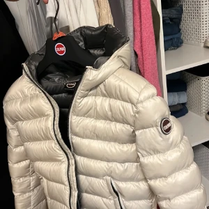 Colmar jacka  - Snygg beige pufferjacka från Colmar med huva och dragkedja framtill. Jackan har en quiltad look, Colmar-logga på ärmen och insida i grått. Perfekt för kalla dagar och riktigt skön att bära.