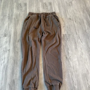 Bruna mjukisbyxor från DEF med snörning - Bruna mjukisbyxor från DEF med elastisk midja och snörning. Byxorna har resår vid bensluten och två sidofickor. Perfekta för en avslappnad stil och tillverkade i mjukt bomullsmaterial.