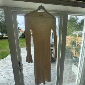 Beige ribbad långklänning - Säljer en krämvit ribbad långklänning med långärmade ärmar och lätt utsvängda muddar. Klänningen har en smickrande slim passform och är tillverkad i ett mjukt stickat material som känns skönt mot huden. Perfekt för dig som gillar stilrena och enkla looks.