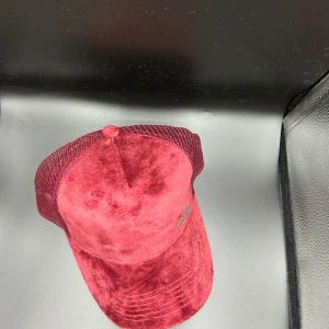 Vinröd keps i sammet från Marciano - Snygg vinröd keps från Marciano med mjuk sammetsfront och mesh på sidorna. Klassisk böjd skärm och metallogo framtill. Perfekt accessoar för en trendig streetstyle-look.