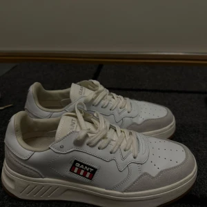 Vita sneakers från GANT - Snygga vita sneakers från GANT med klassisk siluett och perforerade detaljer på tån. Skorna har en vit ovandel i skinn och mocka, samt GANT-logga på sidan. Tjock, vit sula och snörning framtill ger en sportig och fräsch look.