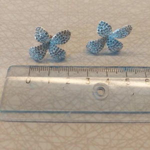 Glittriga blomformade örhängen från SNÖ - Säljer ett par snygga örhängen i form av blommor med fyra kronblad. De är täckta av glittriga stenar i silver och ljusblå toner som verkligen poppar. Perfekt för dig som vill ha något unikt och iögonfallande till din stil.