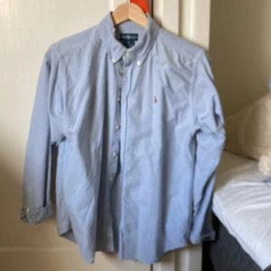 Ljusblå skjorta från Ralph Lauren - Klassisk ljusblå skjorta från Ralph Lauren med button-down krage och broderad logga på bröstet. Skjortan har lång ärm, knappar framtill och är tillverkad i bomull. Perfekt för en clean och stilren look. Skick 9/10 - enda deffekten kan vara lite smuts ovanför loggan på bild 4, men inget som syns om man inte aktivt kollar efter det. Strlk: 18 år. Nypris runt 1000kr