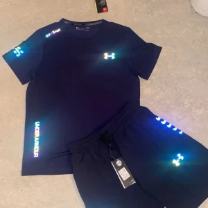 Under Armour set - Snygg mörkblå t-shirt och shorts från Under Armour med korta ärmar och logga på bröste och shortsen. T-shirten har en klassisk rund hals och är gjord i mjukt material som passar perfekt för träning. Diskreta detaljer med reflextryck på sidan och ärmen även på shortsen