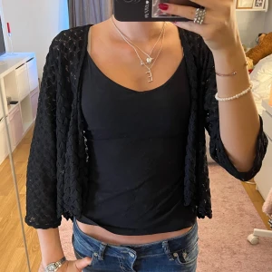 Svart bolerotopp med spetsdetaljer - Säljer en svart bolerotopp med trekvartsärm och snygga spetsdetaljer. Toppen är croppad och har ett luftigt, mönstrat tyg som ger en cool look. Perfekt att slänga över ett linne eller klänning för att lyfta outfiten💕