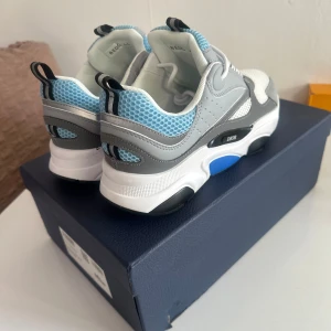 Dior B22 sneakers i blå och grå - Säljer ett par Dior B22 sneakers med chunky sula i vitt, grått och blått. Ovandelen har mesh i blått och vitt, detaljer i grått skinn och svarta inslag. Snygg logga på sidan och på innersulan. Perfekta för dig som gillar statement sneakers med lyxig känsla.
