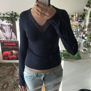 Mörkblå långärmad topp med spets, stretchig  - Mörkblå långärmad topp från Gina Tricot med v-ringning och snygg spetsdetalj runt halsen. Toppens material är mjukt och stretchigt, perfekt att styla med jeans eller kjol. Enkel men ändå elegant design som lyfter din outfit.