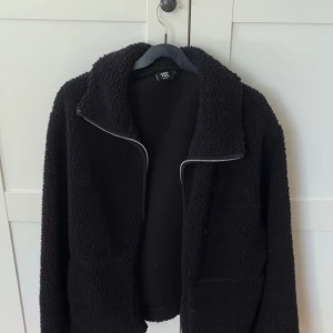 Svart teddyjacka från Lager157 - Mysig svart teddyjacka från Lager 157 i storlek L. Passar mer S/M. Jackan har hel dragkedja framtill, två stora fickor och en hög krage. Perfekt för kyliga dagar när du vill ha en chill och avslappnad stil.