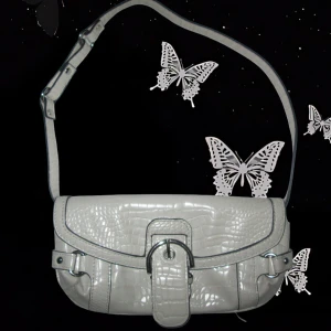 🤍 Vit Y2K krokodil axelväska 🤍 - Axelväska i ljus creme med krokodilpräglad flap, metallspänne och justerbar rem. 🤍 Väskan har metallspännen som lyfter looken.  Liten till medelstor – perfekt för både vardag och utekväll! Obs: Lite smutsig på insidan – inget som syns utifrån, men nämns för transparens.