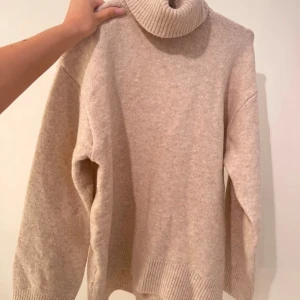 Beige polotröja från BikBok - Supermysig beige polotröja från BikBok i stickad kvalitet. Tröjan har en hög, ribbad polokrage och breda muddar vid ärmslut och nederkant. Passformen är loose och den är perfekt för kyliga dagar. Den är aldrig använd.