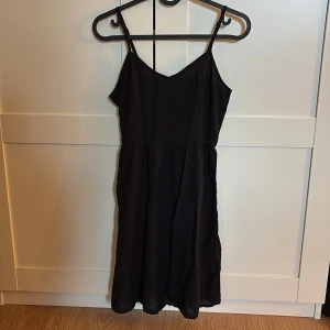 Svart ärmlös kortklänning - En svart, enkel och luftig kortklänning med smala axelband och v-ringad hals. 