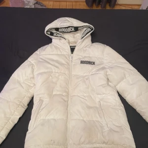 Vit pufferjacka från Hoodrich strl L - Säljer en vit pufferjacka från Hoodrich i storlek L. Jackan har huva med snörning och Hoodrich-logga längs kanten, dragkedja framtill och två fickor. Perfekt för kalla dagar och har en clean streetstyle-look. Kan gå ner i pris vid snabb affär