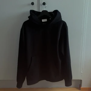 Svart hoodie från Jack & Jones - Svart hoodie från Jack & Jones med klassisk huva och känguruficka framtill. Tröjan har en enkel och clean design, perfekt för dig som gillar en stilren look. Den är storlek L men kan även passa M, säljer för att jag inte använder den så mycket. Den är i nyskick.