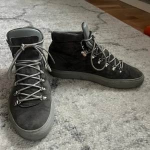 Grå boots från Diemme - Snygga boots från Diemme i grå mocka med matchande grå snörning och robust sula. Skorna har metallöglor för snörningen och en mjuk, vadderad plös i ljusgrått skinn. Perfekta för dig som gillar stilrena och funktionella skor med streetkänsla.