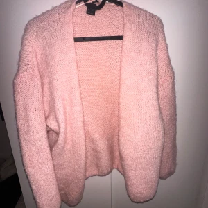 Rosa stickad kofta från Lindex - Mysig och fluffig rosa stickad kofta från Lindex. Koftan har öppen front utan knappar och långa ärmar. Perfekt för lager-på-lager och ger en chill vibe till din outfit.