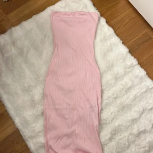 Ljusrosa axelbandslös långklänning Storlek M - Säljer en ljusrosa axelbandslös långklänning i ribbat material. Klänningen är figurnära och har en liten slits baktill för extra rörelsefrihet. Perfekt för dig som gillar en enkel men snygg look med en feminin touch.