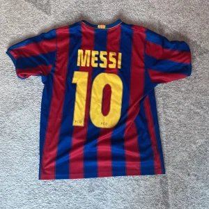FC Barcelona  - Säljer en klassisk FC Barcelona fotbollströja med Messi 10 på ryggen. Tröjan är blå och röd med vertikala ränder, kortärmad och har klubbmärke samt Unicef-tryck på bröstet. Perfekt för dig som älskar fotboll och vill hylla en av de största.