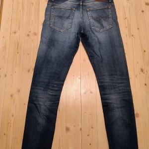 Tiger of Sweden blå jeans - Snygga blå jeans från Tiger of Sweden med klassisk femficksdesign och kontrastsömmar. Jeansen har en rak passform och är tillverkade i slitstarkt denimtyg. Perfekta för dig som gillar stilrena och tidlösa jeans med en modern touch.                                                                    Jeansen är i toppskick. Storlek W31 L34