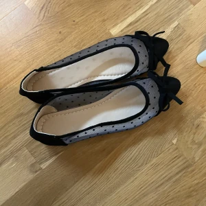 Svarta ballerinaskor med prickigt nät - Snygga ballerinaskor i svart med transparent mesh och små svarta prickar. Skorna har en söt rosett framtill och platt sula. Perfekta för dig som gillar en feminin och trendig stil.