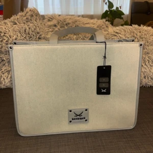 Ljusbeige handväska från Sansibar - Stilren ljusbeige handväska från Sansibar med rektangulär form, dubbla handtag och detaljer i ljusgrått skinn. Väskan har ett stort huvudfack och innerficka med dragkedja. Perfekt för dig som gillar minimalistisk design och vill ha plats för allt du behöver.