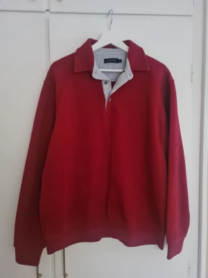 Röd pikétröja från Allan Clark - Röd pikétröja från Allan Clark i storlek L. Tröjan har klassisk krage med smala blåvita ränder och knappar framtill
