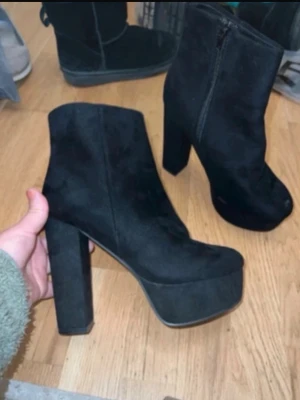 Svarta platåstövletter med hög klack - Säljer ett par svarta stövletter i mocka-look med rejäl platåsula och hög, bred klack. Skorna har rund tå och dragkedja på sidan för enkel påtagning. Perfekta för dig som vill ha extra höjd och en edgy stil. Dem är väldigt bekväma på, vänster fot har en liten typ fläck/ detalj som man lär kunna fixa med sån mock-färg ifall man vill fixa det själv. Då jag inte är så händig men det är så pass litet att det inte märks.