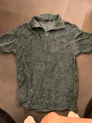 Grön frotté polotopp med ficka - Mjuk grön polotopp från Weekday i frotté med korta ärmar och en bröstficka. Perfekt för en avslappnad och chill stil. Kragen ger en lite sportig känsla och materialet är riktigt skönt mot huden.