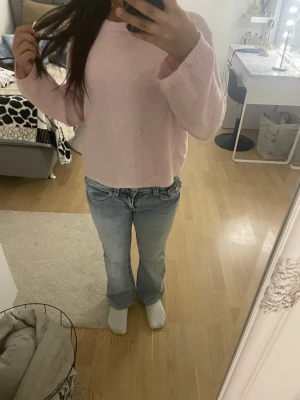 Ljusblå bootcut jeans med knapp ficka  - Säljer ett par ljusblå jeans med bootcut-modell och snygga broderade detaljer på bakfickorna. Jeansen har låg midja och klassisk femficksdesign. Perfekta för dig som gillar en avslappnad och trendig look.