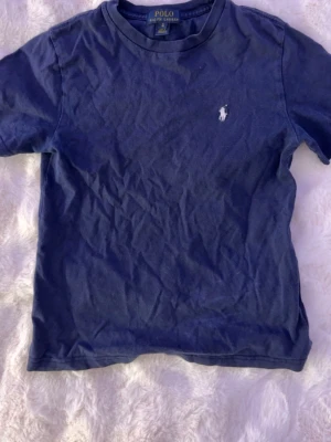 Mörkblå t-shirt från Polo Ralph Lauren - Klassisk mörkblå t-shirt från Polo Ralph Lauren med rund halsringning och den ikoniska vita broderade loggan på bröstet. Tillverkad i mjuk bomull och har en enkel, stilren design som funkar till allt. Är som en xxs!