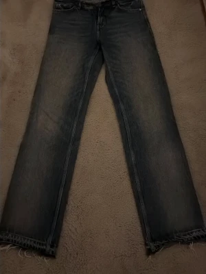 Blå raka jeans från Zara - Säljer ett par blå jeans från Zara i rak modell med råa, fransiga benslut. Jeansen har klassisk femficksdesign och är tillverkade i slitstarkt bomullsmaterial. Perfekta för en avslappnad och trendig look.