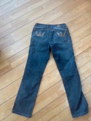Blåa jeans med broderade fickor - Säljer ett par blå jeans från JOOP! med snygga broderade detaljer i guld på bakfickorna. Klassisk femficksmodell med raka ben och normal passform. Jeansen har knappgylf och är tillverkade i slitstarkt denimtyg.