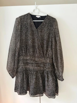 Leopardmönstrad kortklänning med volang - Säljer en kort klänning med leopardmönster i svart, beige och brunt. Klänningen är helt oanvänd och därför i fint skick. Den är från ginas barnavdelning så därför storlek 158/164 så skulle därför säga runt xs.😊