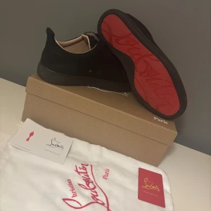 Svarta  Christian Louboutin skor - Säljer ett par svarta sneakers från Christian Louboutin i mocka med klassisk röd sula och diskret logga på innersulan. Skorna har rund tå, svarta skosnören och beige innersida i skinn. Kommer med originalkartong, dustbag och certifikat. Funkar i st 41-42. Kontakta vid frågor om skon eller pris 😊