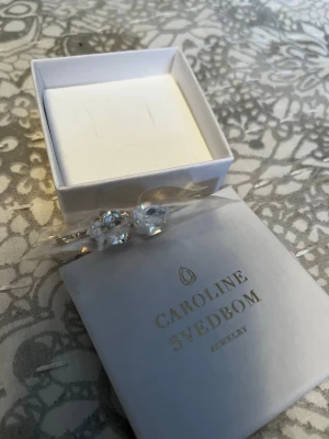 Caroline Svedbom örhängen - Säljer ett par Carlotta Clasp örhängen från Caroline Svedbom i färgen Golden Shadow. Örhängena har gnistrande ljusgula kristaller och guldfärgade detaljer. Perfekta för att ge din look lite extra bling!