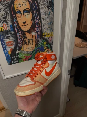 Nike Jordan 1 High Orange/Vit - Säljer ett par Nike Jordan 1 High i orange och vitt. Skorna har klassisk hög siluett, orange swoosh och detaljer, samt snörning. Ovandelen är i skinn och textil, med rund tå och platt sula. Perfekta för dig som gillar retrostil och streetwear.