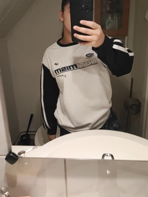 Vit och marinblå sweatshirt med tryck - Säljer en oversized vit och svart sweatshirt från Optimism med tryck på bröstet och svarta ärmar med vita ränder. Tröjan har rund hals och är tillverkad i mjuk bomullsmix. Perfekt för en chill och sportig stil. Storlek S och taggen är kvar. 